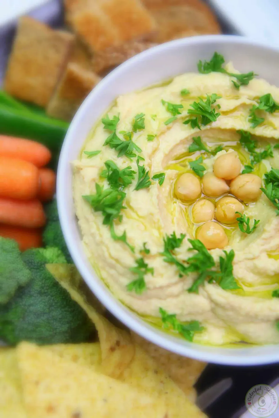 Bowl of 5 minute creamy hummus topped with whole chickpeas, olive oil and parsley