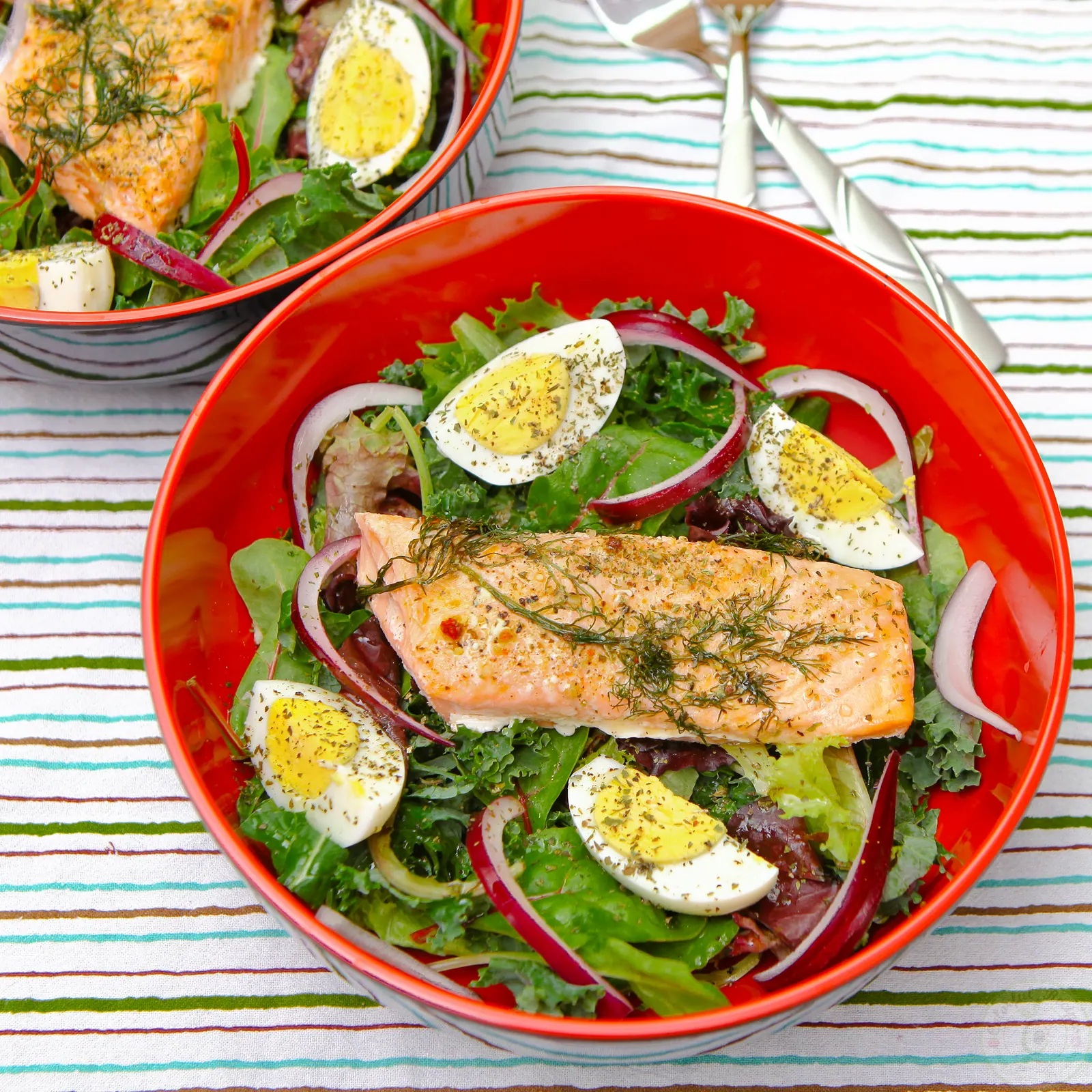 Quick leftover salmon salad with boiled eggs, red onion and greens in a red bowl