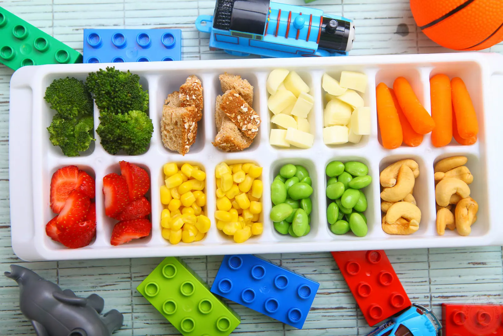Toddler approved ice cube tray colorful buffet with broccoli, strawberries, corn, edamame and cashews