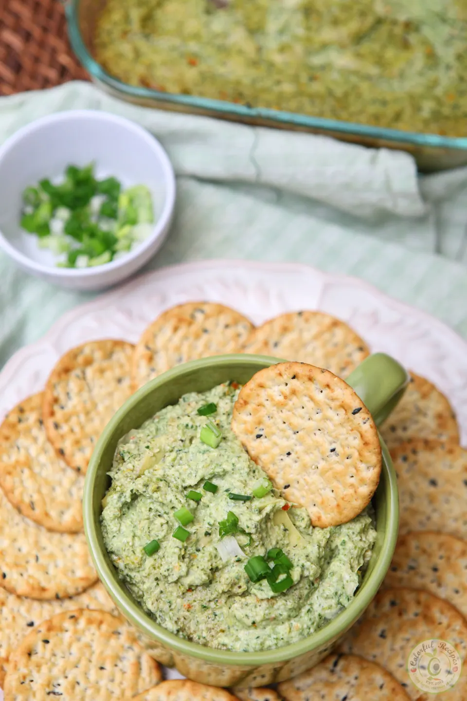 Hot and hearty artichoke spinach dip in a casserole dish with crackers