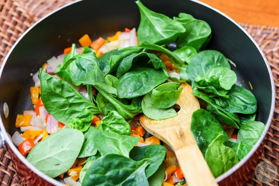 Wilting fresh spinach with sautéed peppers in a skillet