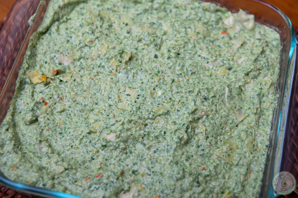 Unbaked artichoke spinach dip spread in a casserole dish