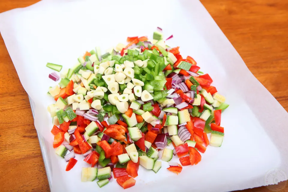 Chopped red and green bell peppers, zucchini and red onion on a parchment-lined baking sheet