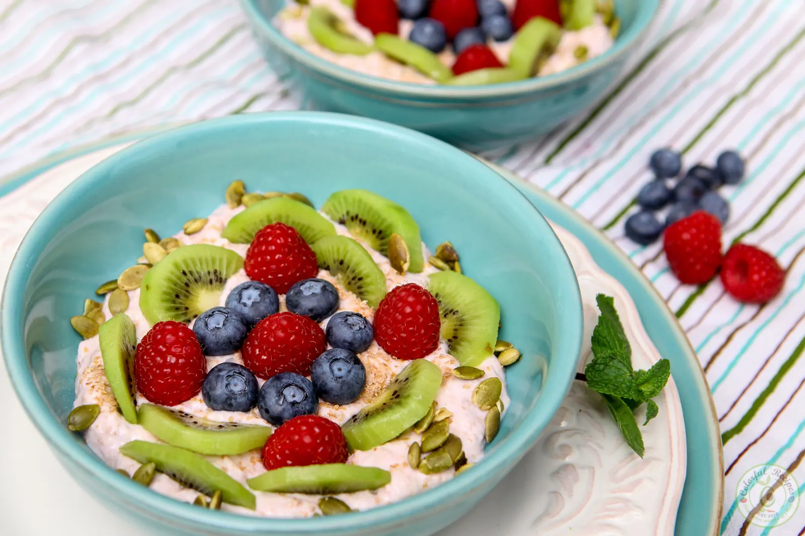 Banana yogurt fruit breakfast bowl topped with kiwi slices, raspberries, blueberries and pumpkin seeds