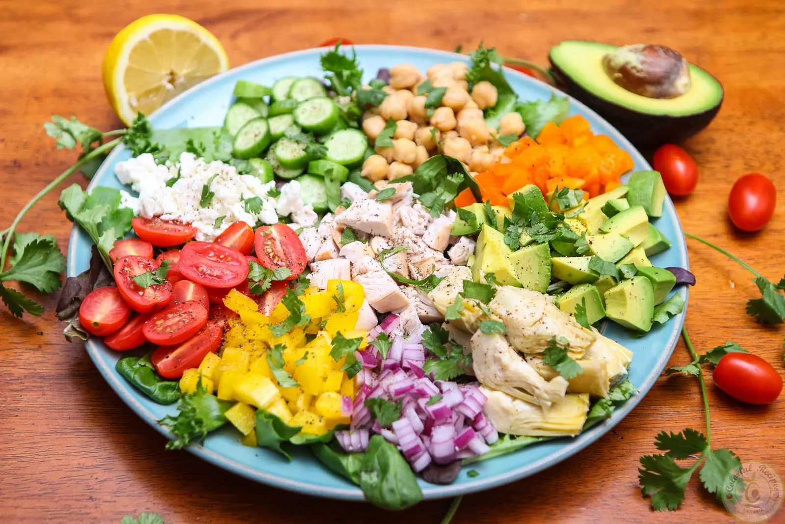 Colorful fresh chopped salad with chicken, chickpeas, avocado, feta and veggies arranged in sections