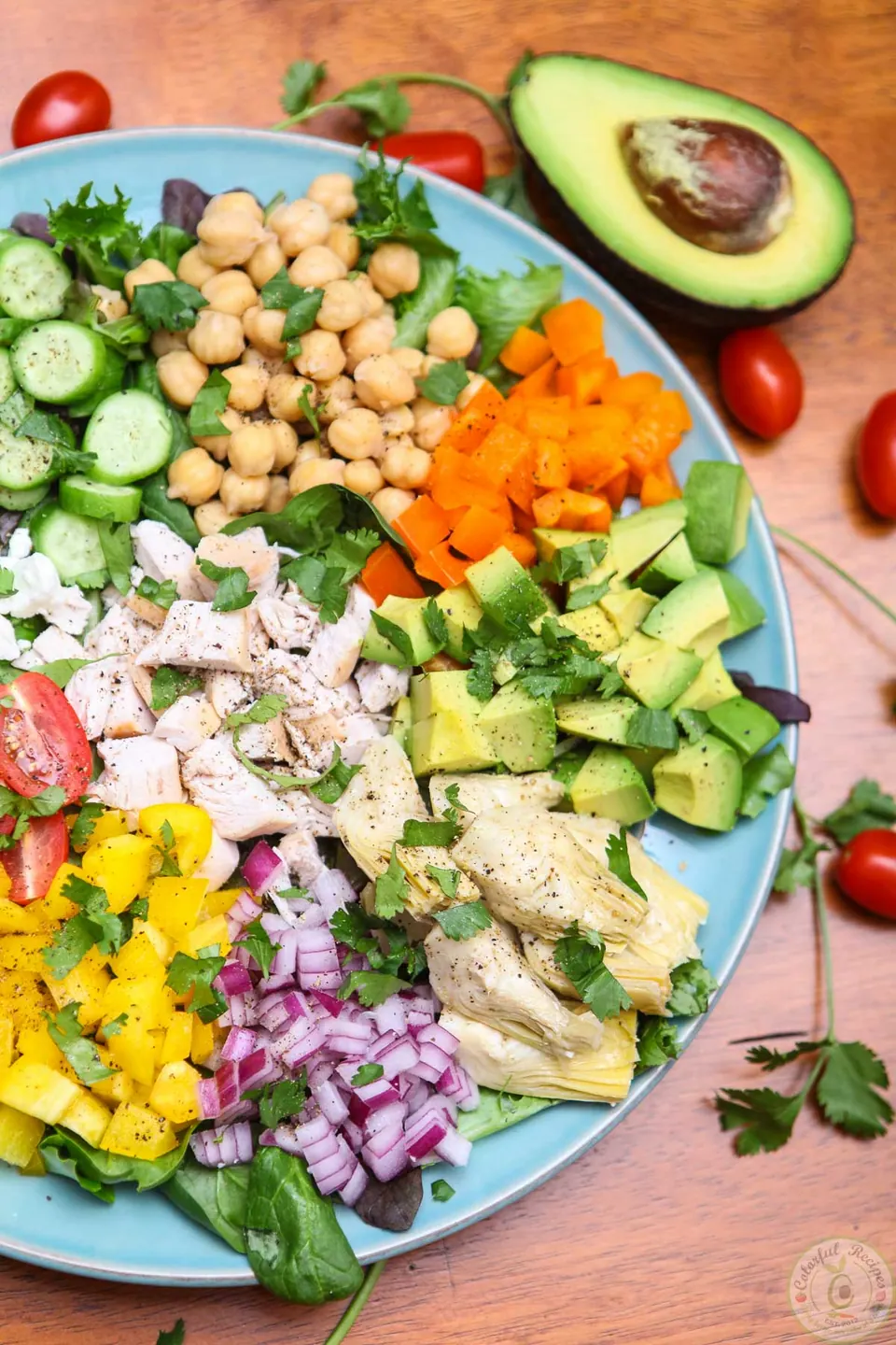 Colorful fresh chopped salad with chicken, chickpeas, avocado, feta and tomatoes on a blue platter