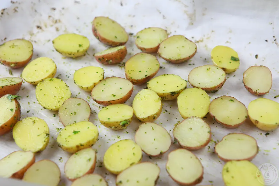 Halved baby potatoes on a parchment-lined baking sheet before roasting