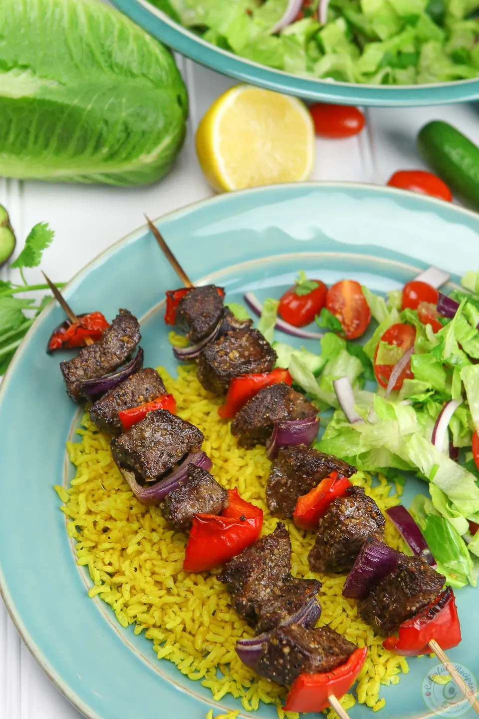 Two broiled beef kabobs on turmeric rice with a fresh green salad