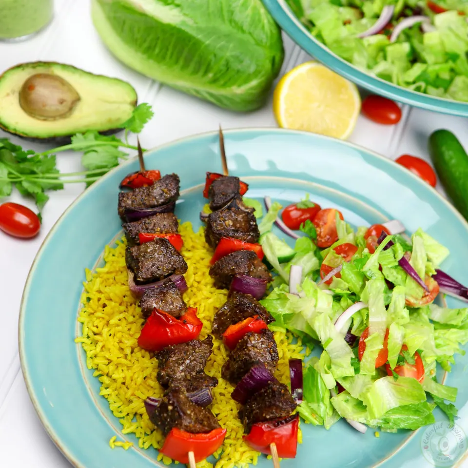 Broiled beef kabobs served on turmeric rice with salad, avocado and lemon
